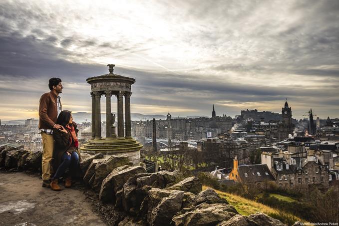 Calton Hill, Edinburgh. View over the historic city buildings and rooftops. A young couple taking in the view over the city in winter.