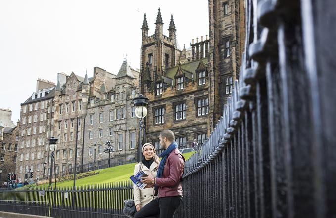 Young couple standing at an iron fence outside the Scottish National Gallery, Edinburgh, Scotland.