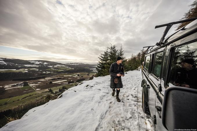 A Scottish guide in kilt and sporran on a highland road by a four by four vehicle.