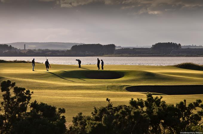 Silhouette of people golfing on The Old Course golf grounds in St Andrews. Grey sky, shaded  view of grounds. Hole 12.